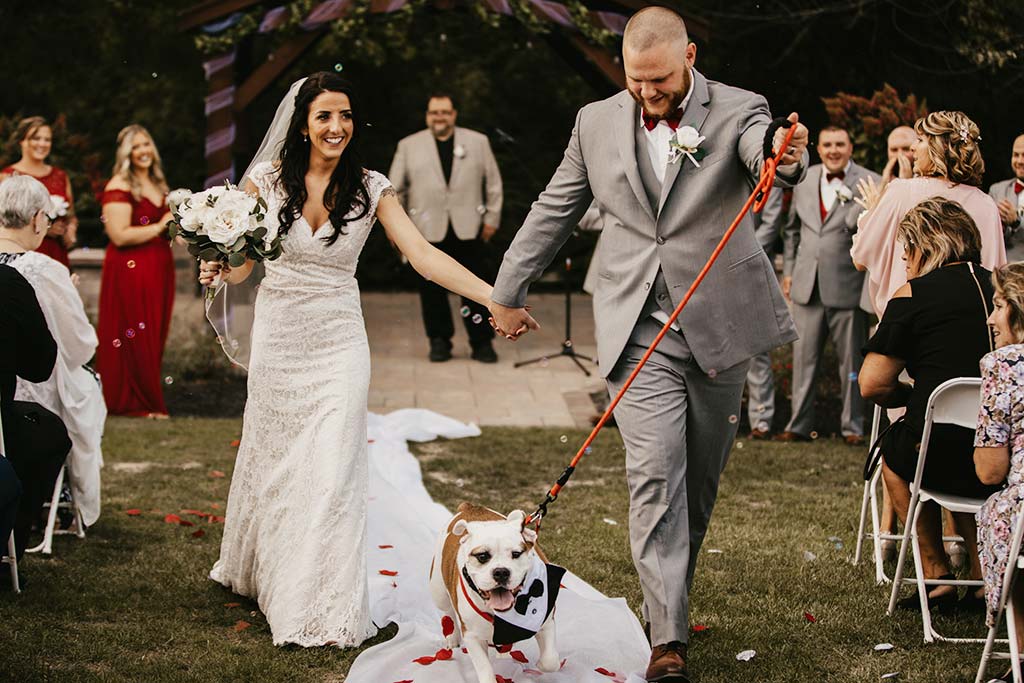 husband and wife walking down the aisle with a dog